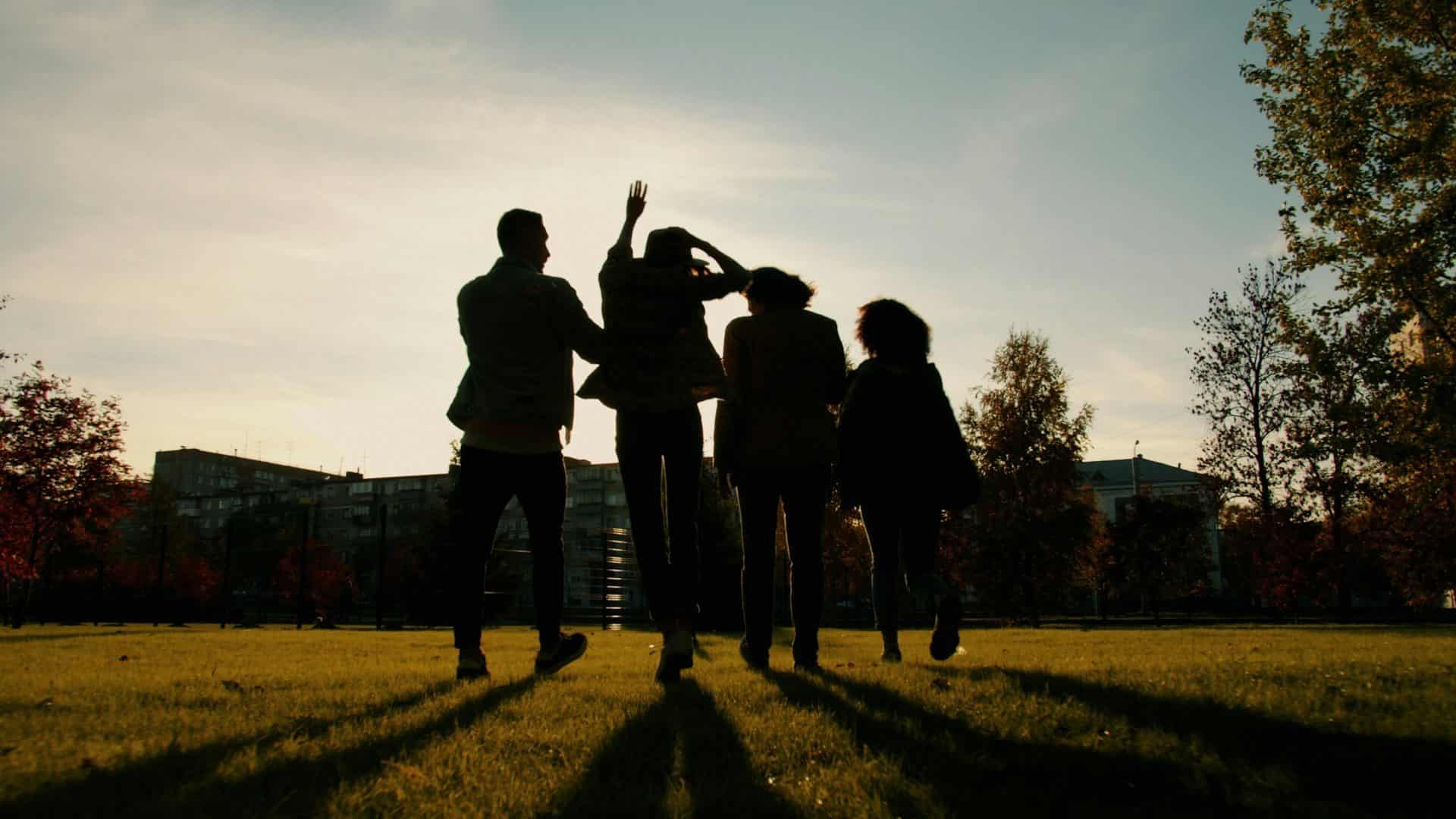 Quatre silhouettes marchant dans un parc au soleil couchant